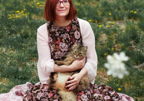 woman in white cardigan sitting on pink textile on green grass field during daytime