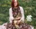 woman in white cardigan sitting on pink textile on green grass field during daytime